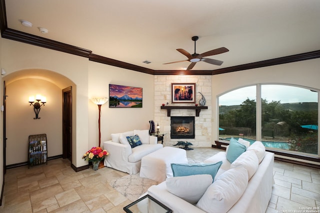 living room with crown molding, ceiling fan, and a stone fireplace