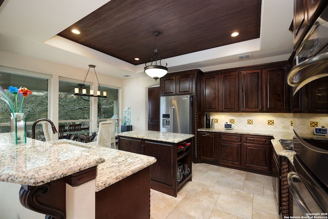 kitchen with a kitchen island with sink, hanging light fixtures, a tray ceiling, and high end fridge