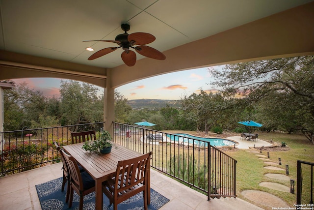 patio terrace at dusk featuring a fenced in pool, ceiling fan, and a lawn