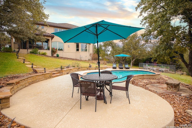 patio terrace at dusk featuring a fenced in pool and a lawn