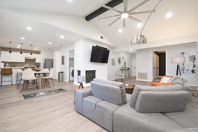 living room with beam ceiling, washer / dryer, high vaulted ceiling, and light wood-type flooring