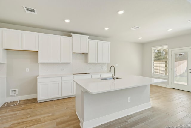 kitchen featuring sink, a kitchen island with sink, white cabinetry, tasteful backsplash, and black electric stovetop