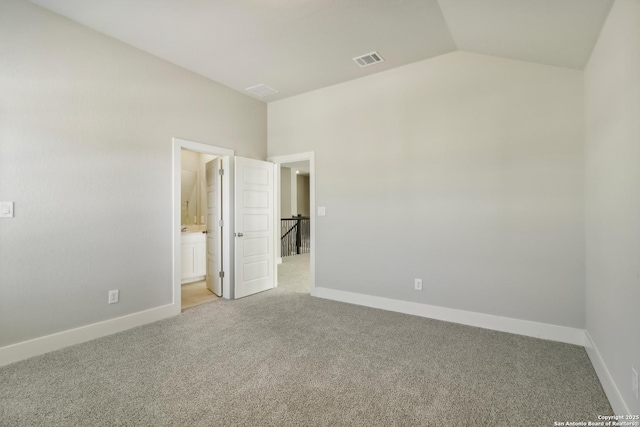 unfurnished bedroom featuring vaulted ceiling, light carpet, and ensuite bath