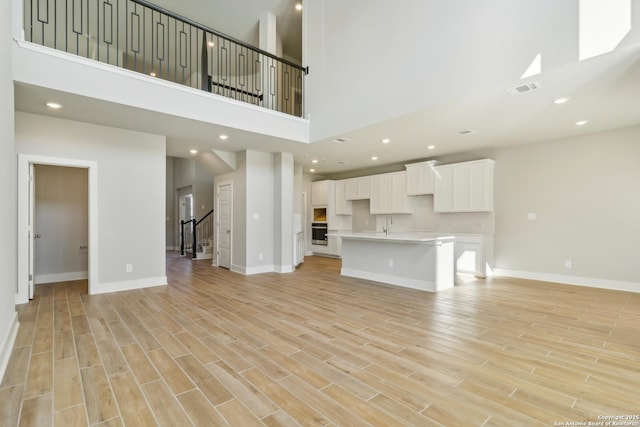 unfurnished living room featuring a high ceiling and light hardwood / wood-style floors