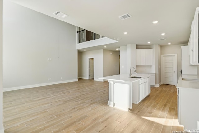 kitchen featuring a kitchen island with sink, sink, white cabinets, and light hardwood / wood-style flooring