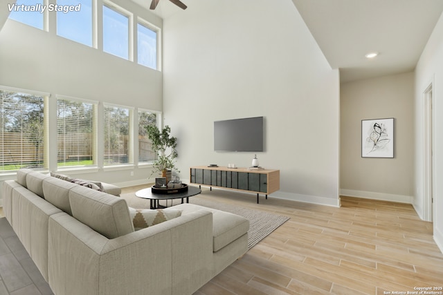 living room featuring a high ceiling, ceiling fan, and light hardwood / wood-style floors