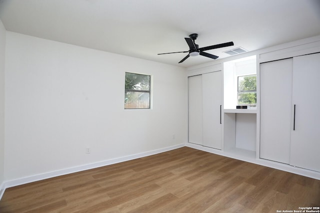 unfurnished bedroom featuring multiple closets, hardwood / wood-style floors, and ceiling fan