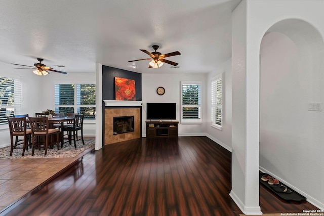 living room with a tile fireplace, dark wood-type flooring, and ceiling fan