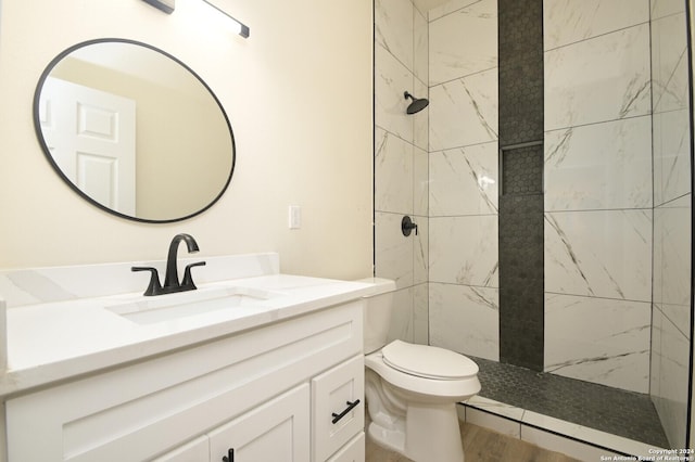 bathroom featuring a tile shower, vanity, and toilet