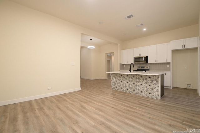 kitchen with a kitchen island with sink, stainless steel appliances, tasteful backsplash, white cabinets, and light wood-type flooring