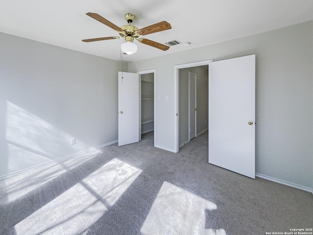 unfurnished bedroom with a walk in closet, carpet flooring, and ceiling fan