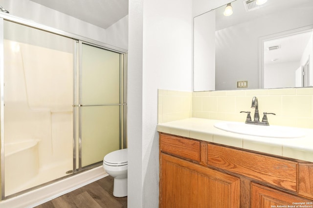 bathroom with toilet, wood-type flooring, vanity, a shower with door, and backsplash