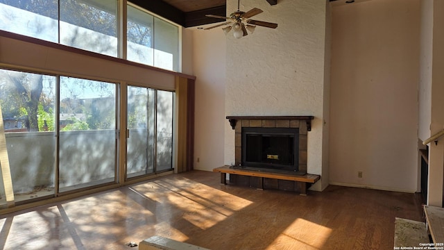 unfurnished living room featuring a tile fireplace, a towering ceiling, hardwood / wood-style floors, and ceiling fan