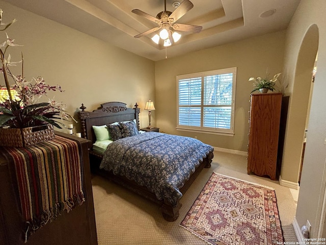 carpeted bedroom with a raised ceiling and ceiling fan