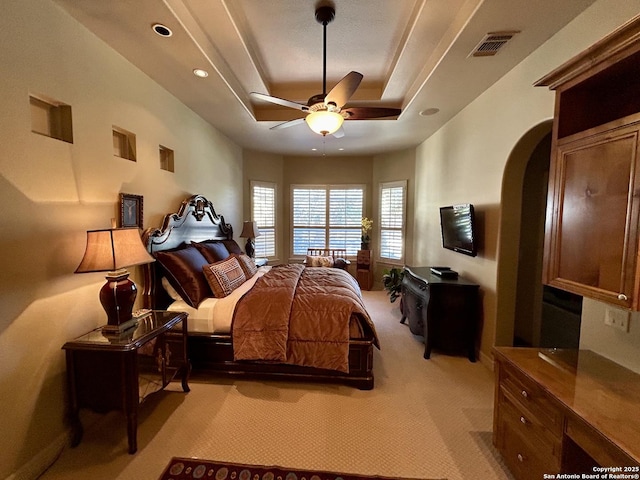 bedroom with a tray ceiling, light colored carpet, and ceiling fan