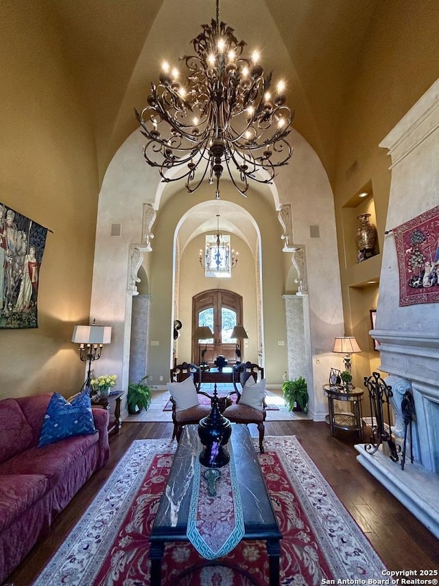 living room featuring dark wood-type flooring, a towering ceiling, an inviting chandelier, and french doors