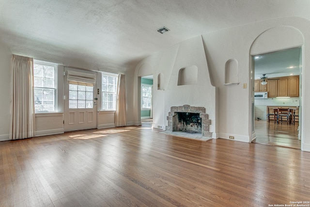 unfurnished living room featuring ceiling fan, wood-type flooring, and a textured ceiling