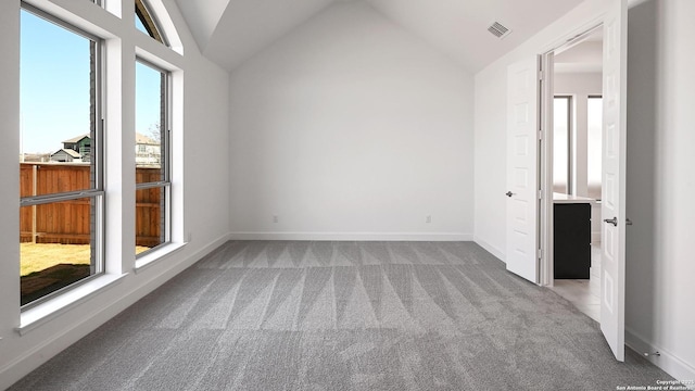 carpeted empty room with baseboards, lofted ceiling, and visible vents