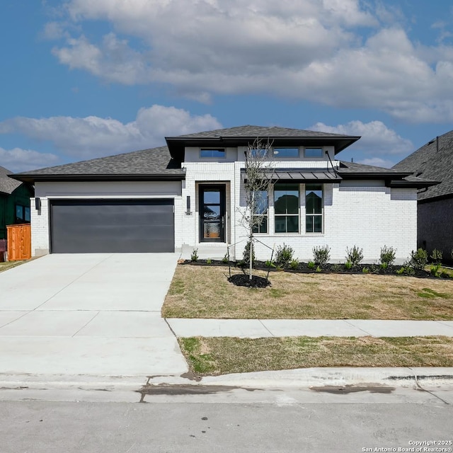 prairie-style home featuring brick siding, concrete driveway, a garage, and a front lawn