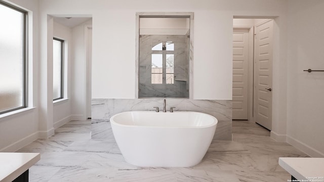 bathroom with baseboards, marble finish floor, a freestanding tub, and vanity