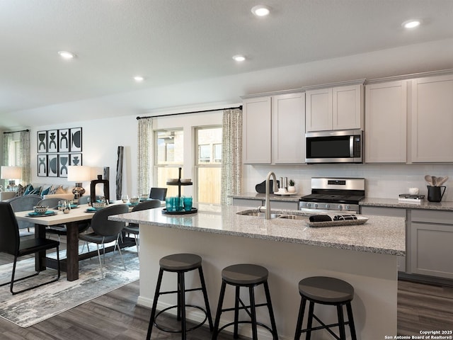 kitchen featuring stainless steel appliances, dark hardwood / wood-style floors, a center island with sink, and a kitchen bar