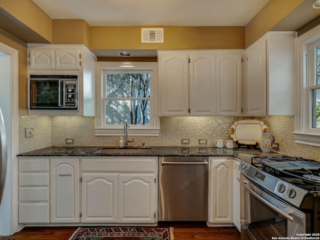 kitchen featuring appliances with stainless steel finishes, white cabinetry, sink, dark stone countertops, and backsplash