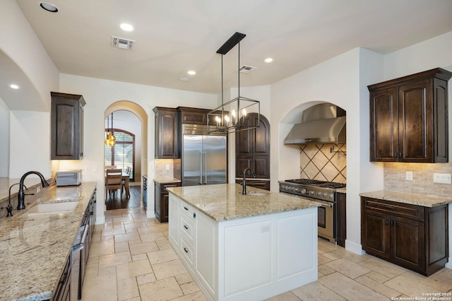 kitchen featuring premium appliances, a sink, visible vents, white cabinets, and wall chimney exhaust hood