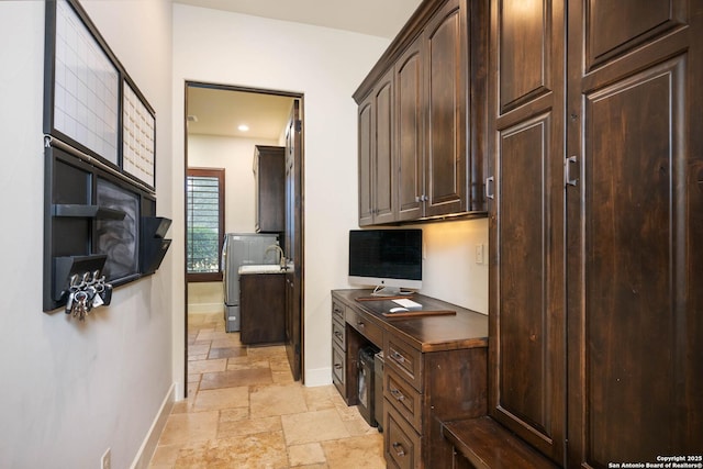 kitchen featuring dark brown cabinetry, stone tile floors, baseboards, built in desk, and dark countertops