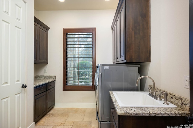 laundry room featuring a sink, baseboards, cabinet space, washer / clothes dryer, and stone tile flooring