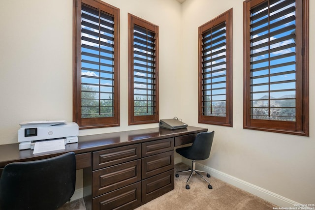 office space featuring a wealth of natural light, light colored carpet, baseboards, and built in study area