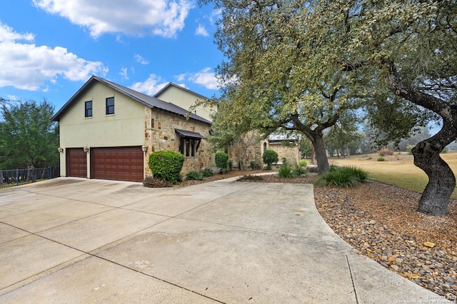 view of front of property featuring an attached garage, fence, driveway, stone siding, and stucco siding