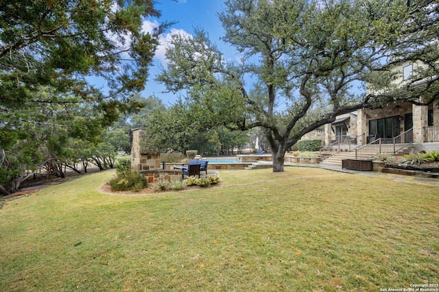 view of yard featuring stairs, an outdoor stone fireplace, and an outdoor pool