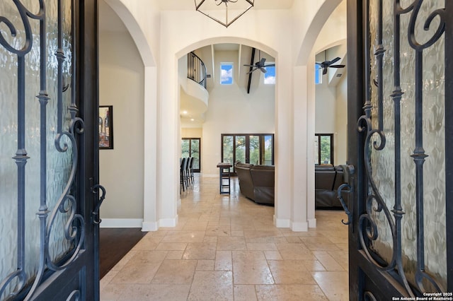 foyer entrance featuring baseboards, arched walkways, a ceiling fan, a towering ceiling, and stone tile flooring