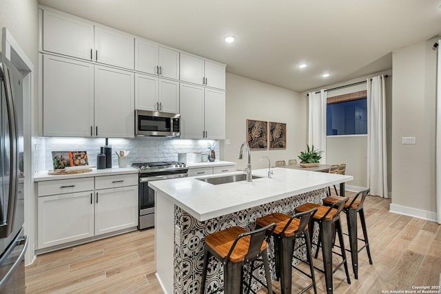 kitchen featuring sink, white cabinetry, stainless steel appliances, light hardwood / wood-style floors, and a kitchen bar