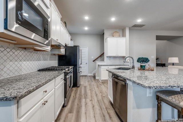 kitchen featuring sink, appliances with stainless steel finishes, white cabinetry, a kitchen breakfast bar, and light stone counters