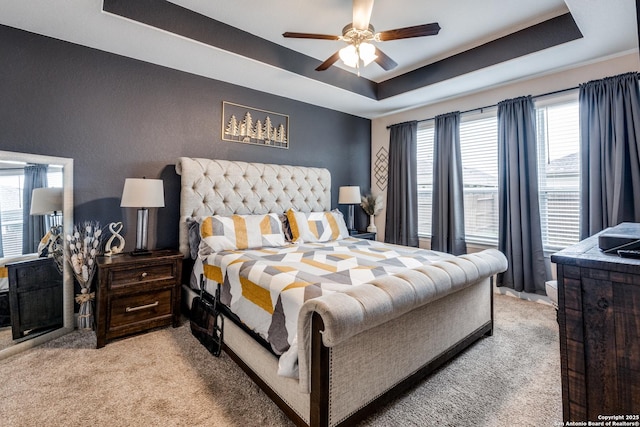 bedroom with light colored carpet, ceiling fan, and a tray ceiling