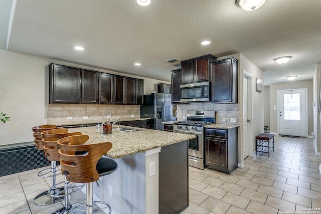 kitchen featuring light tile patterned floors, a breakfast bar area, appliances with stainless steel finishes, light stone counters, and an island with sink