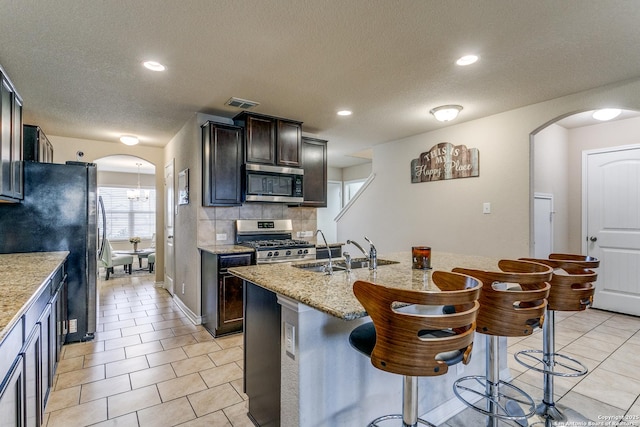 kitchen with a breakfast bar, sink, light stone counters, appliances with stainless steel finishes, and a kitchen island with sink