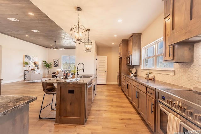 kitchen with appliances with stainless steel finishes, a breakfast bar area, hanging light fixtures, a kitchen island with sink, and light wood-type flooring