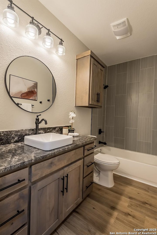 full bathroom with vanity, hardwood / wood-style floors, tiled shower / bath combo, and toilet