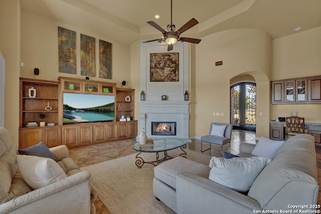 living room with ceiling fan, a towering ceiling, a fireplace, and french doors