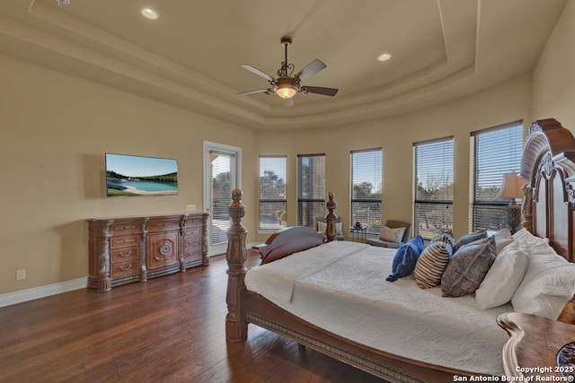 bedroom with a raised ceiling, dark wood-type flooring, and ceiling fan