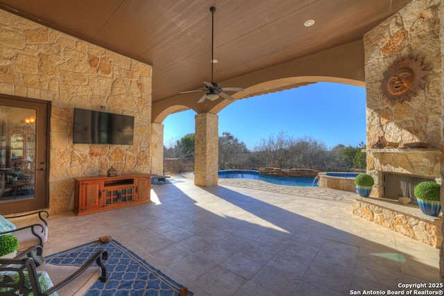 view of patio featuring ceiling fan, an in ground hot tub, and an outdoor stone fireplace