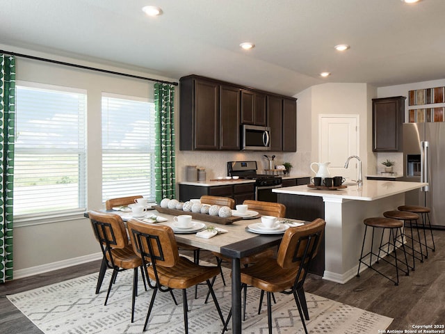 kitchen featuring appliances with stainless steel finishes, a kitchen island with sink, dark brown cabinetry, and decorative backsplash