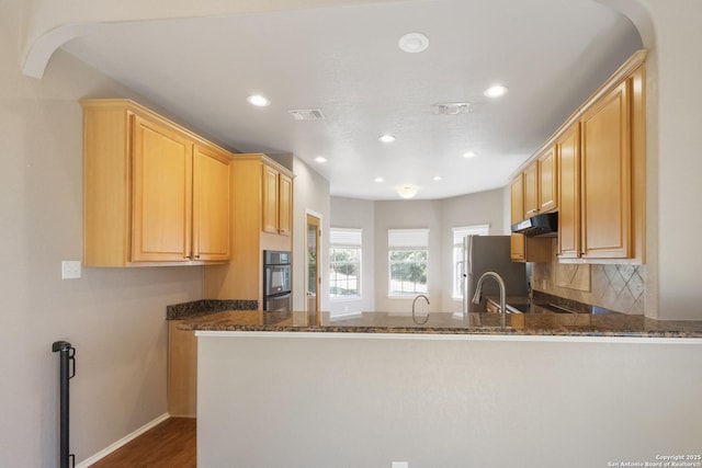 kitchen featuring dark stone countertops, light brown cabinetry, and kitchen peninsula