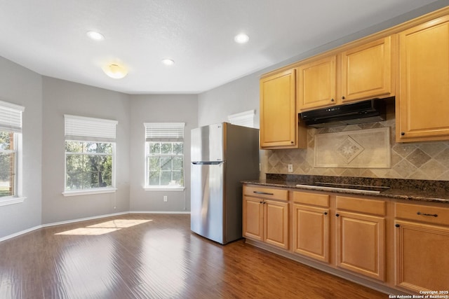 kitchen featuring black electric stovetop, stainless steel refrigerator, dark stone counters, and wood-type flooring