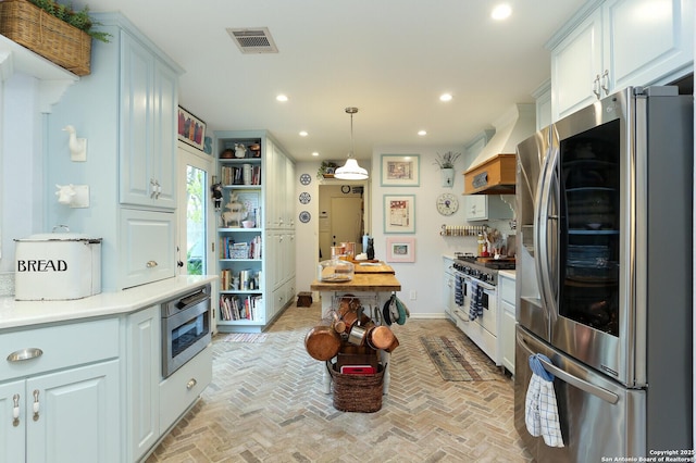 kitchen featuring white cabinetry, decorative light fixtures, premium range hood, and appliances with stainless steel finishes