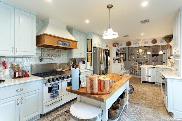 kitchen with premium range hood, pendant lighting, white cabinetry, stainless steel fridge, and double oven range