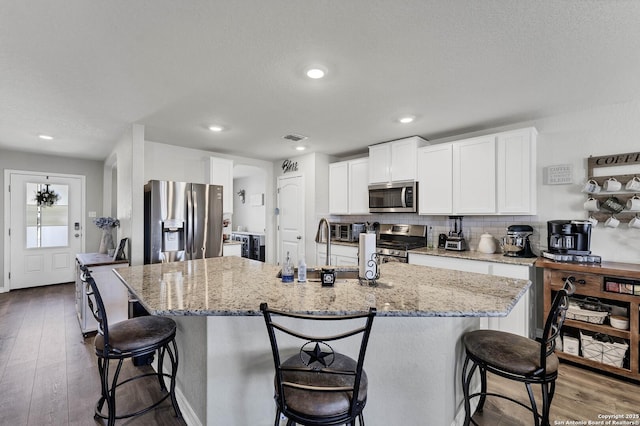 kitchen with white cabinetry, a center island with sink, appliances with stainless steel finishes, hardwood / wood-style flooring, and decorative backsplash