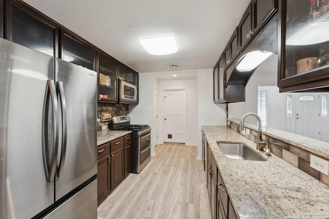 kitchen with tasteful backsplash, sink, light stone counters, stainless steel appliances, and light wood-type flooring